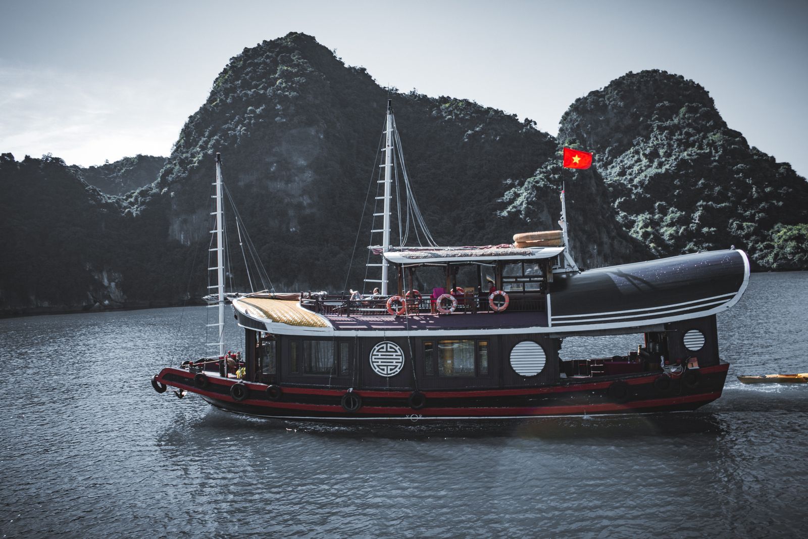 Wooden boat on calm water between limestone cliffs, Halong Bay